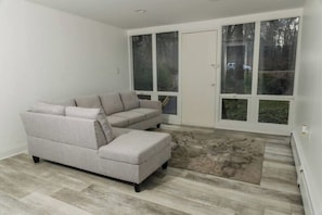 A room with a sectional sofa, large windows, and a patterned rug.