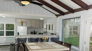 Una cocina moderna con armarios blancos, un comedor con mesa de madera y sillas oscuras, y un ventilador de techo.
