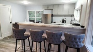 Una cocina moderna con una isla central, taburetes de bar y un ventanal que proporciona luz natural.