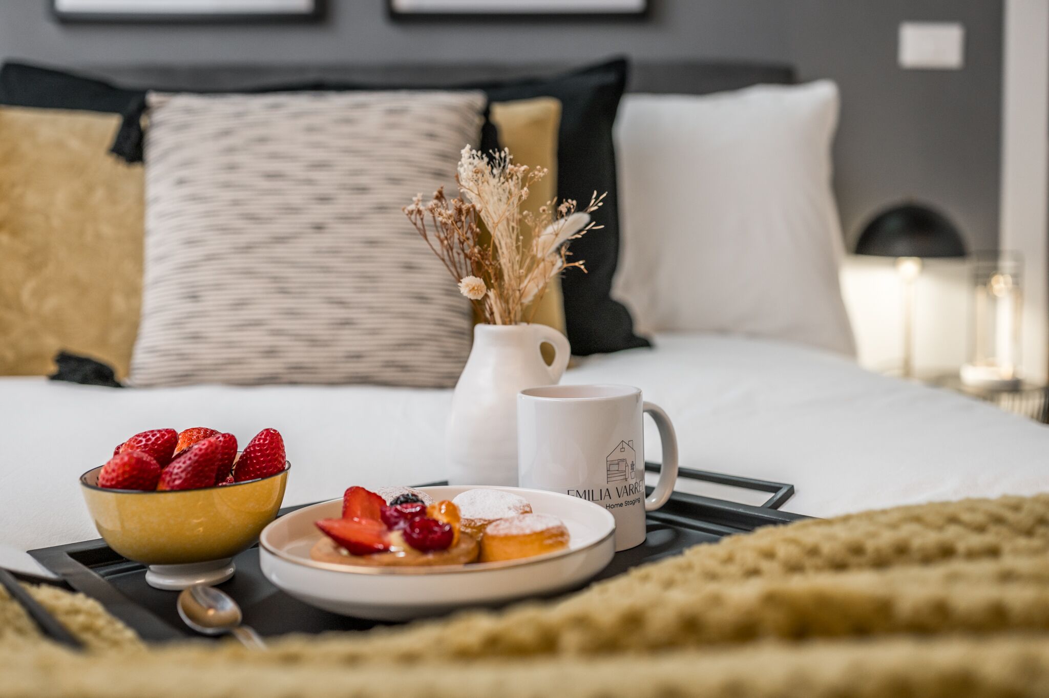 Un petit-déjeuner joliment présenté, disposé sur un plateau : un bol de fraises, une assiette de viennoiseries, une tasse blanche et un vase avec des fleurs séchées.
