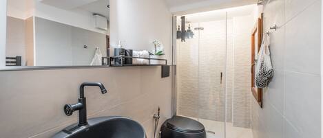 A modern bathroom with a large black sink, a mirror, and a walk-in shower.
