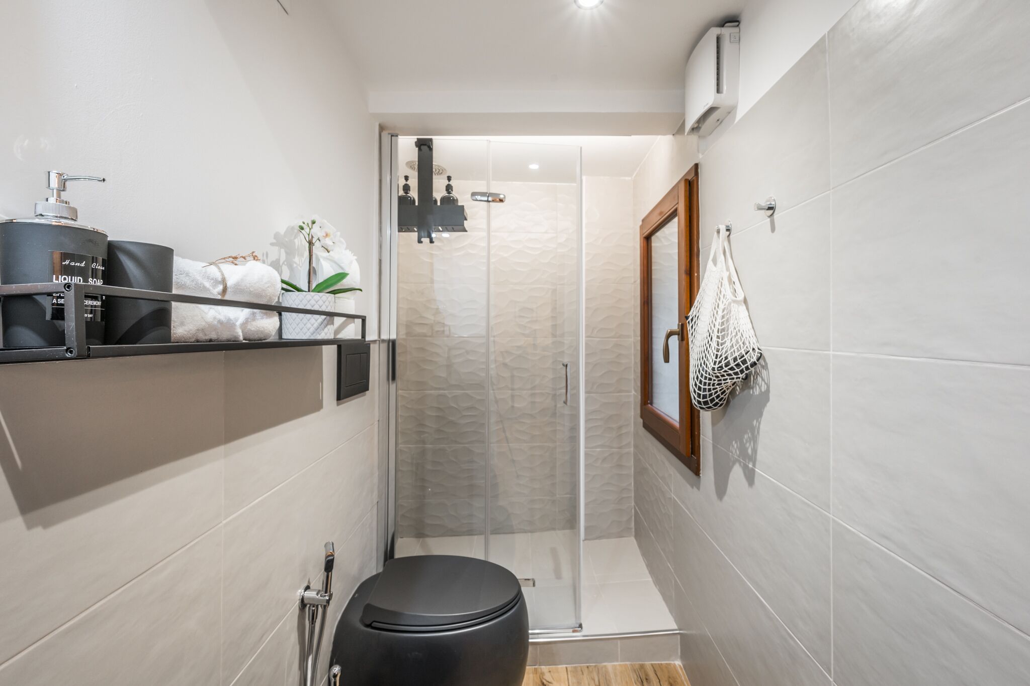 Une salle de bain moderne équipée d’une douche, de toilettes et d’une étagère où sont rangés les produits de toilette.