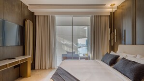 Une chambre d’hôtel moderne dotée d’un grand lit, d’un téléviseur à écran plat, d’un bureau et d’une porte-fenêtre coulissante donnant sur un balcon.