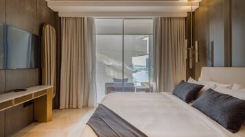 A modern hotel room with a large bed, a flat-screen TV, a desk, and a sliding glass door leading to a balcony.