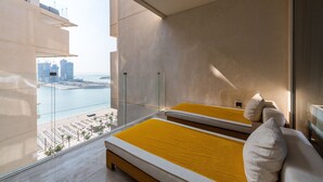 Une chambre d’hôtel moderne dotée d’un grand balcon, d’un lit avec une literie jaune et offrant une vue sur le paysage urbain et l’eau.