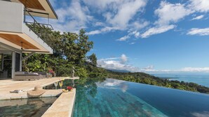 Ein moderner Infinity-Pool mit klarem, blauem Wasser, einer Holzterrasse und Blick auf den Ozean.