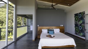 Een moderne slaapkamer met een groot bed, een plafondventilator en uitzicht op groen door grote ramen.