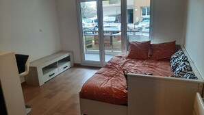 A bedroom with a bed, a bench, and a sliding glass door leading to a balcony. - Studio de 22m 2 (Etrembières)