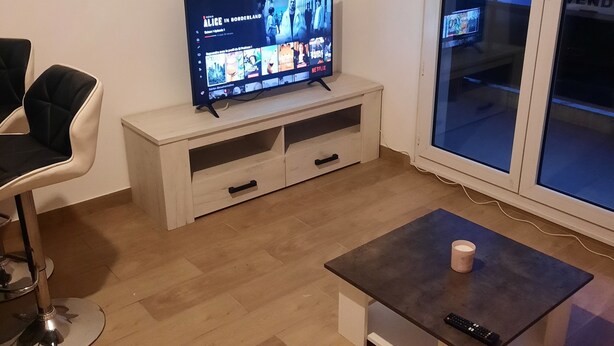 A living room with a TV on a wooden stand, a coffee table, a chair, and a sliding glass door leading outside. - Studio de 22m 2 (Etrembières)