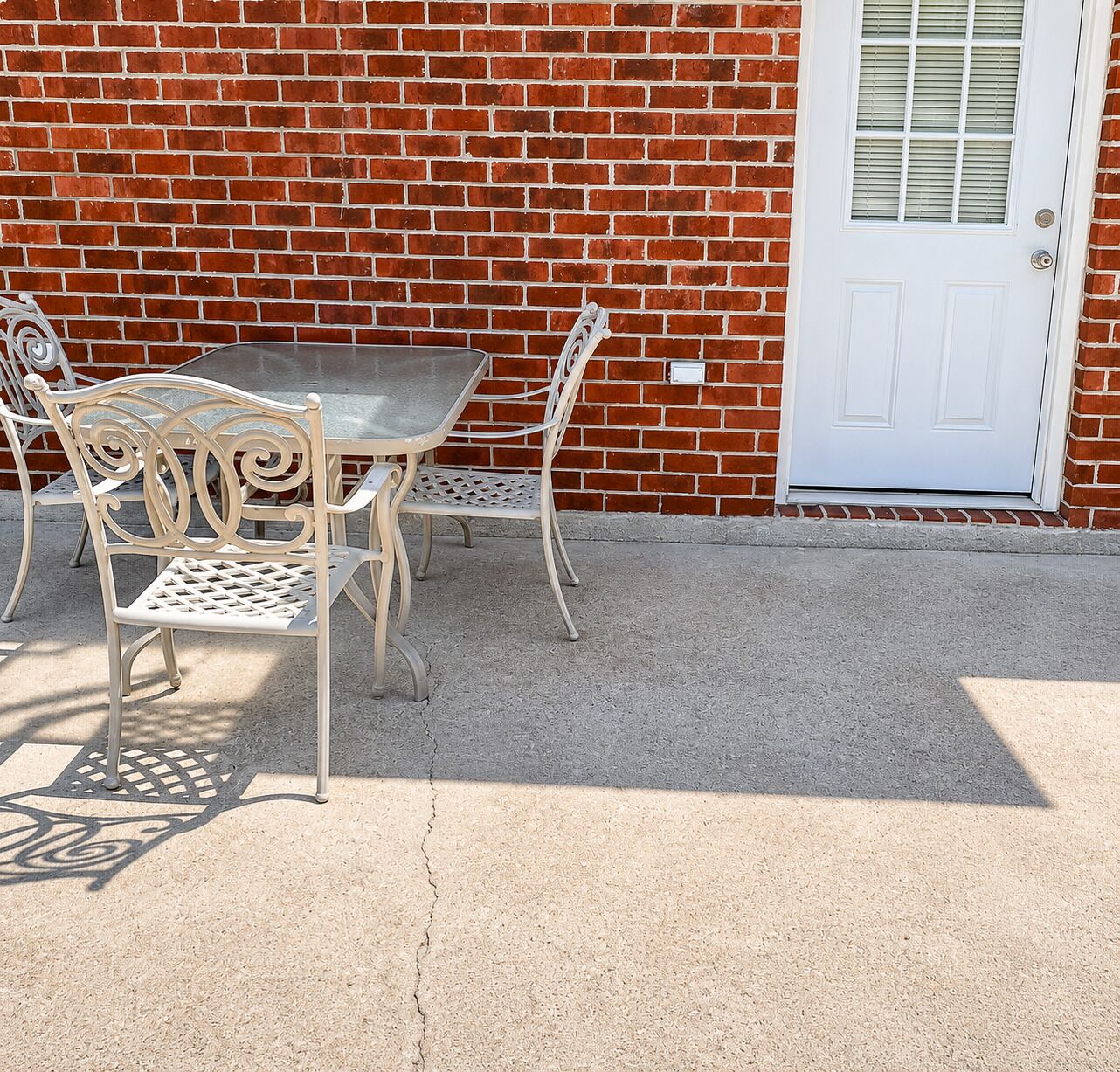 A patio with a table and two chairs, a white door, and a brick wall.