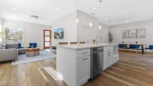 Een moderne keuken met een centraal eiland, houten vloeren en een eethoek met blauwe stoelen.