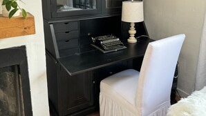 A compact workspace with a dark wooden desk, a white chair, a lamp, and a bookshelf with books. - Cozy Historical Cottage In Petaluma (Petaluma)