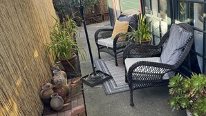 A patio with wicker furniture, potted plants, and a green umbrella. - Cozy Historical Cottage In Petaluma (Petaluma)
