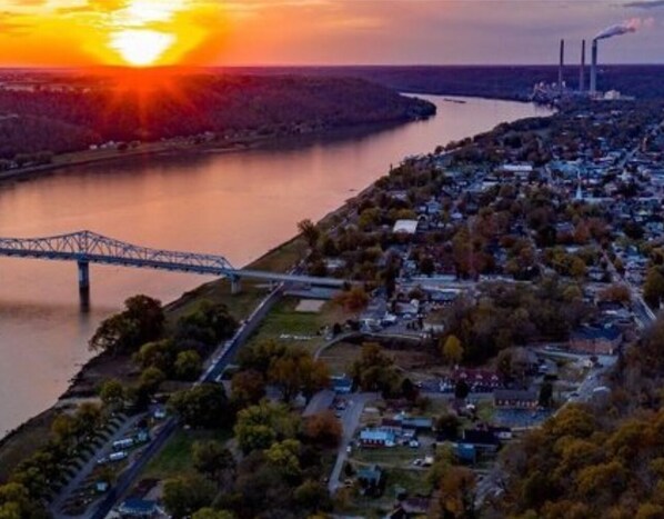 An aerial view of a town with a bridge over a river, industrial buildings, and a sunset.