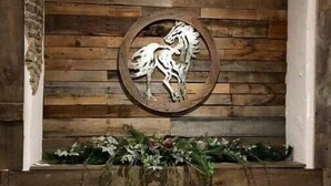 Paredes rústicas com escultura de cavalo em madeira e um vaso com folhagem.