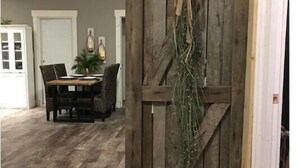 Quarto com porta de madeira, mesa de jantar com cadeiras e uma planta pendurada.