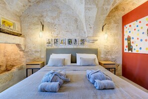 A bedroom with a stone wall, a bed with two pillows, two bedside tables, and a red wall with a colorful painting.