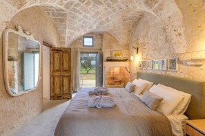 A rustic bedroom with a stone wall, a wooden door, a bed with white linens, and a small window.