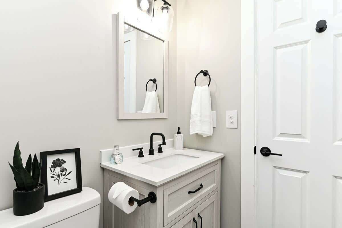 A modern bathroom with a white sink, black faucet, and a framed picture of flowers on the counter.