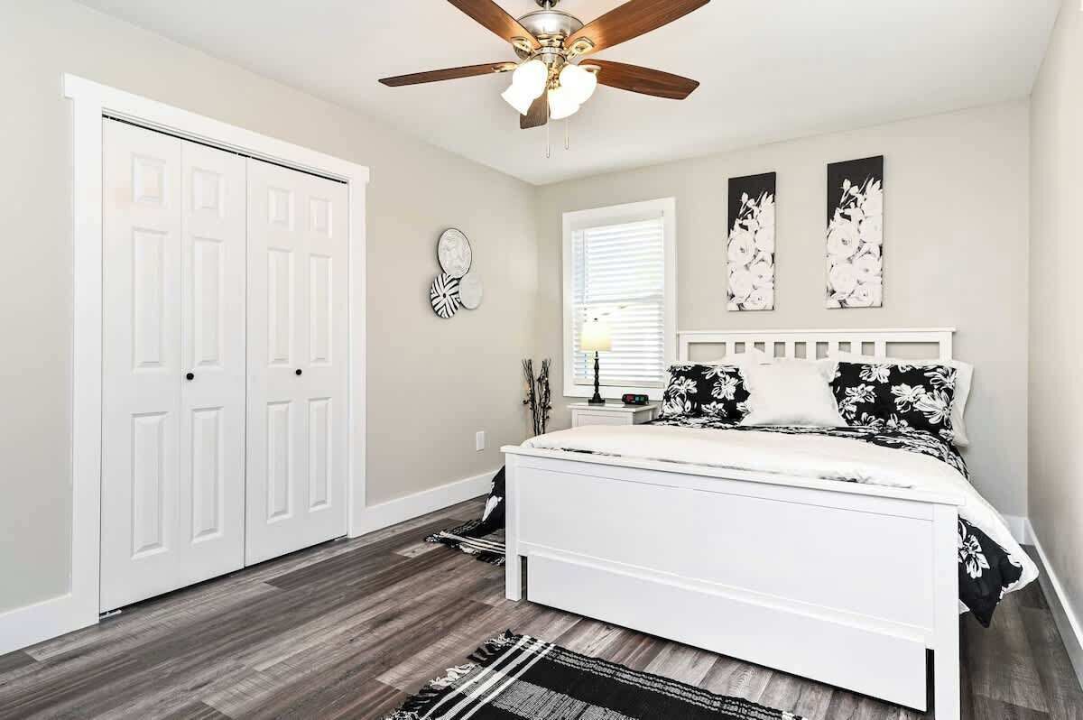 A bedroom with a bed, a ceiling fan, a window with blinds, and a door.