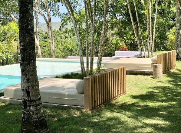 Un espace aménagé au bord de la piscine, avec une clôture en bois, des chaises longues et une vue sur un paysage naturel.