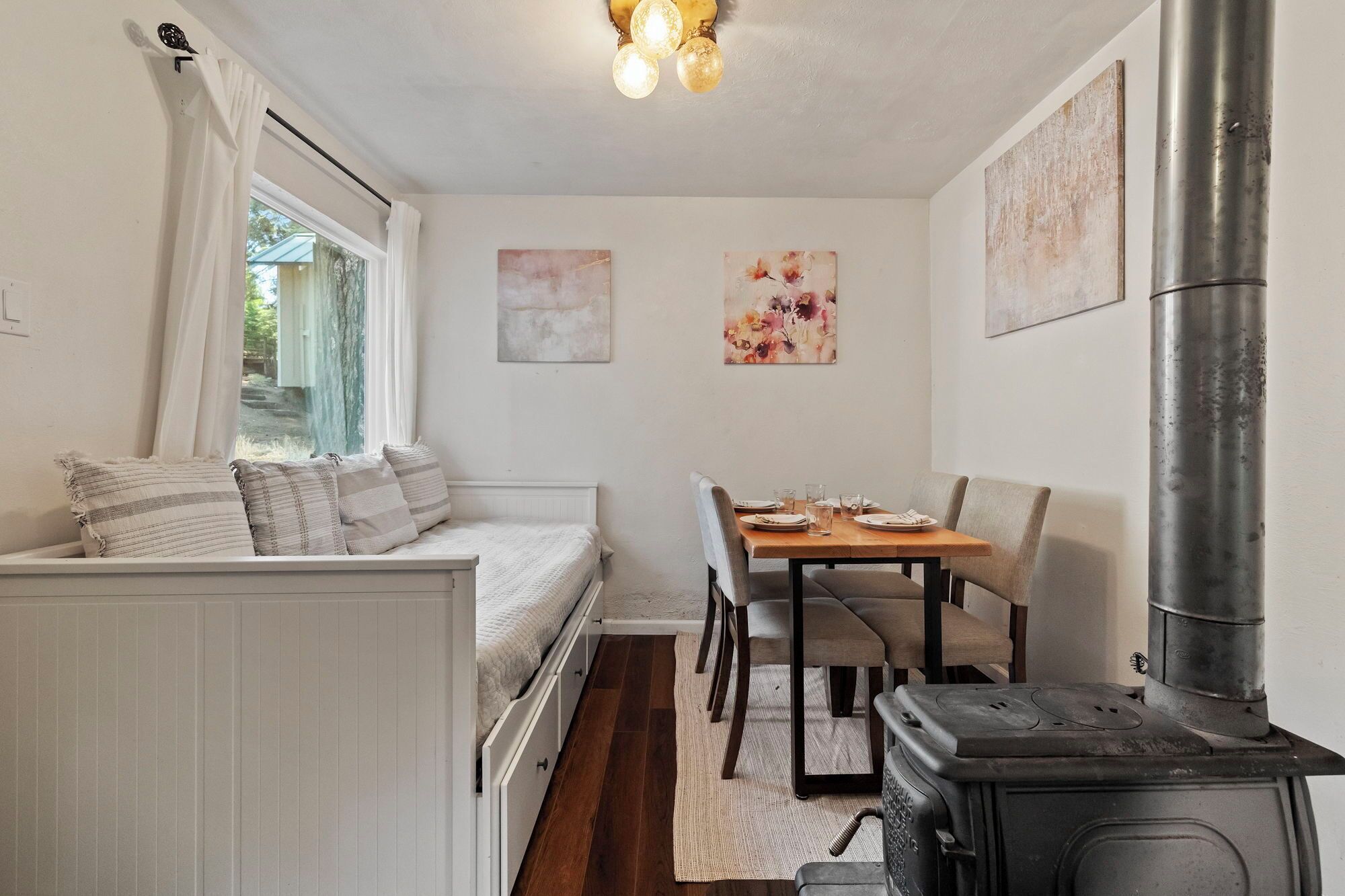 A cozy room with a bed, a dining table with chairs, a stove, and artwork on the walls.