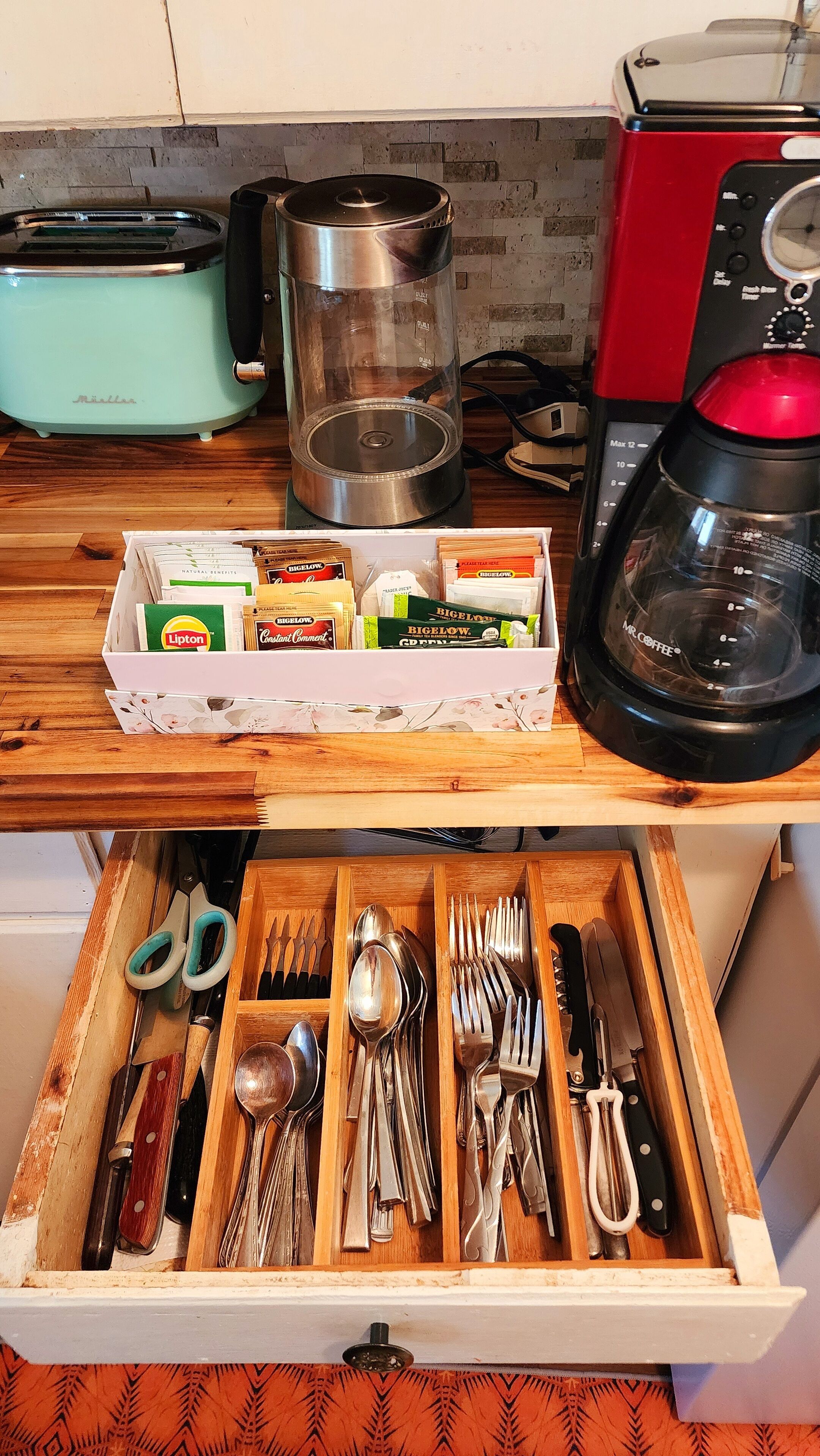 Una cocina con tostadora, cafetera y un cajón con utensilios.