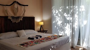 A neatly made bed with a colorful blanket, a bedside lamp, and a macrame wall hanging.
