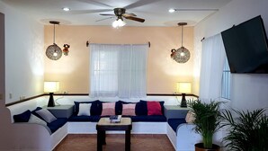 A living room with a sofa, two lamps, a ceiling fan, and a TV mounted on the wall.