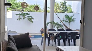 A modern living room with a sofa, a coffee table, and a view of an outdoor patio area with chairs and a pool.