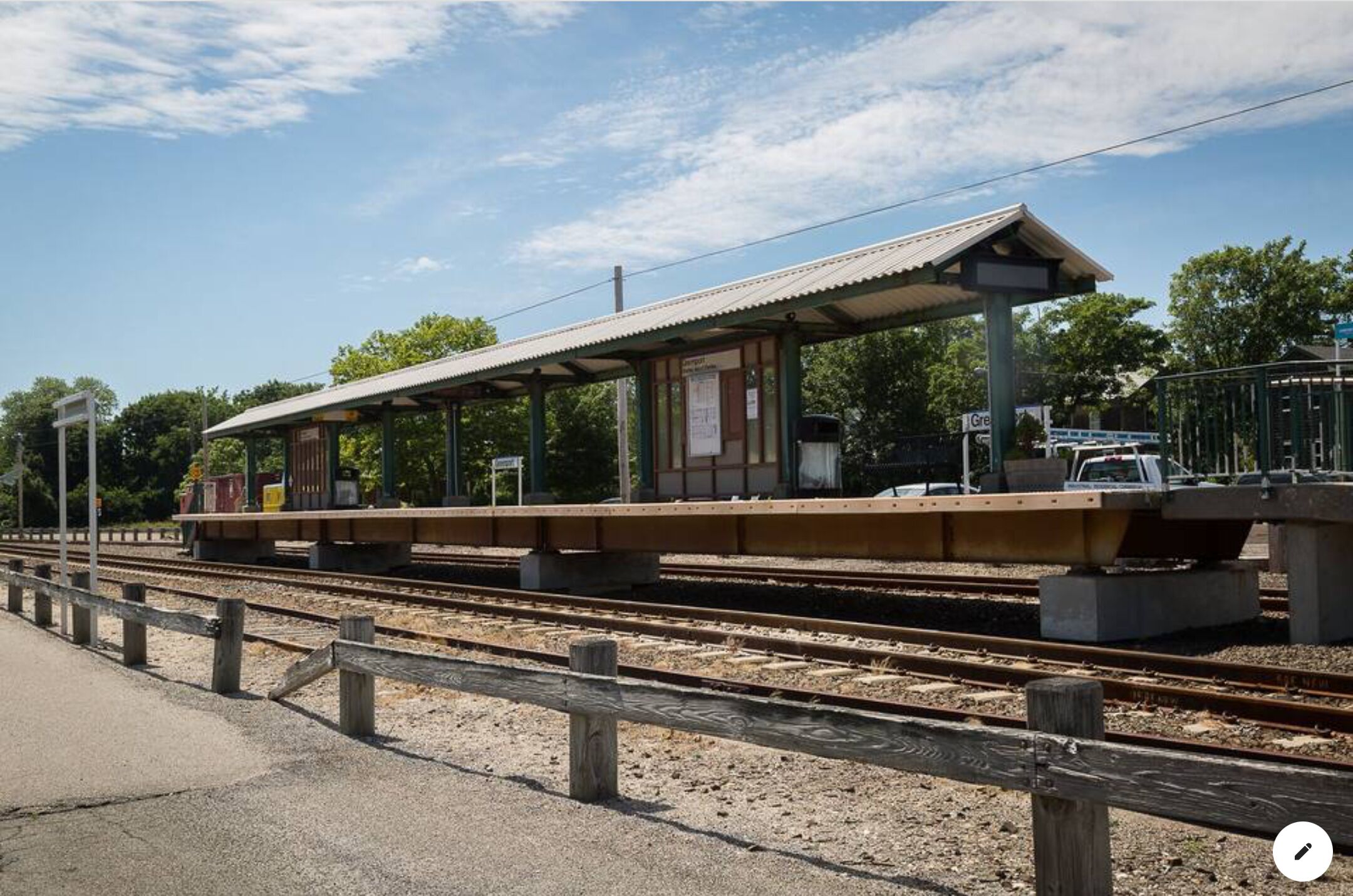 Ein Bahnsteig mit überdachtem Wartebereich, Gleisen und einem Zaun.
