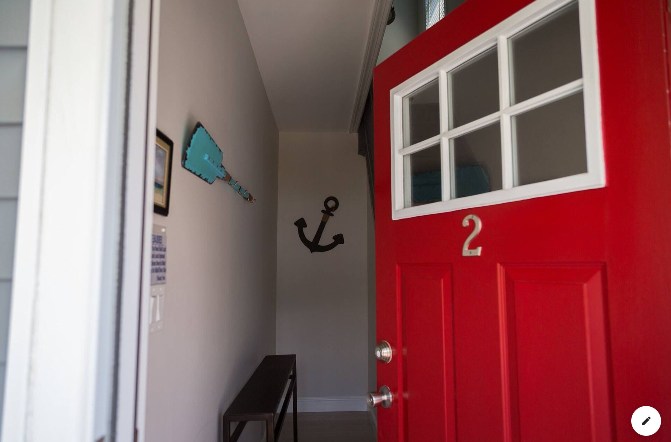 A red door with the number 2, a small bench, and a wall with a blue anchor decoration.
