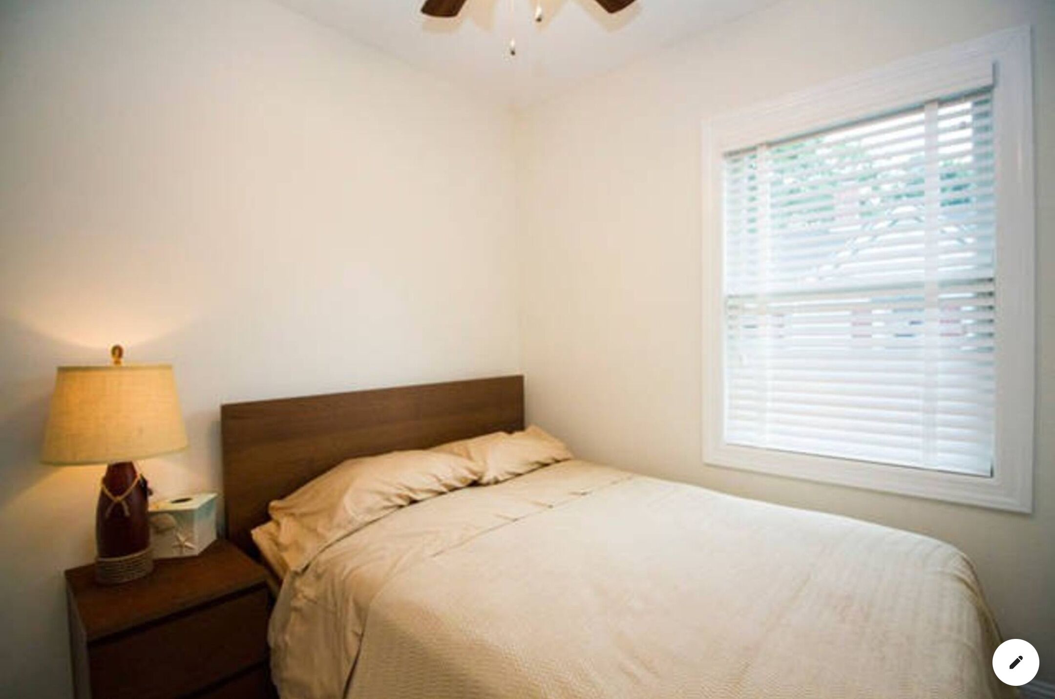 Un dormitorio con una cama individual, una mesita de noche con lámpara y una ventana con persianas.