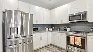 A modern kitchen with stainless steel appliances, white cabinets, and a grey backsplash.