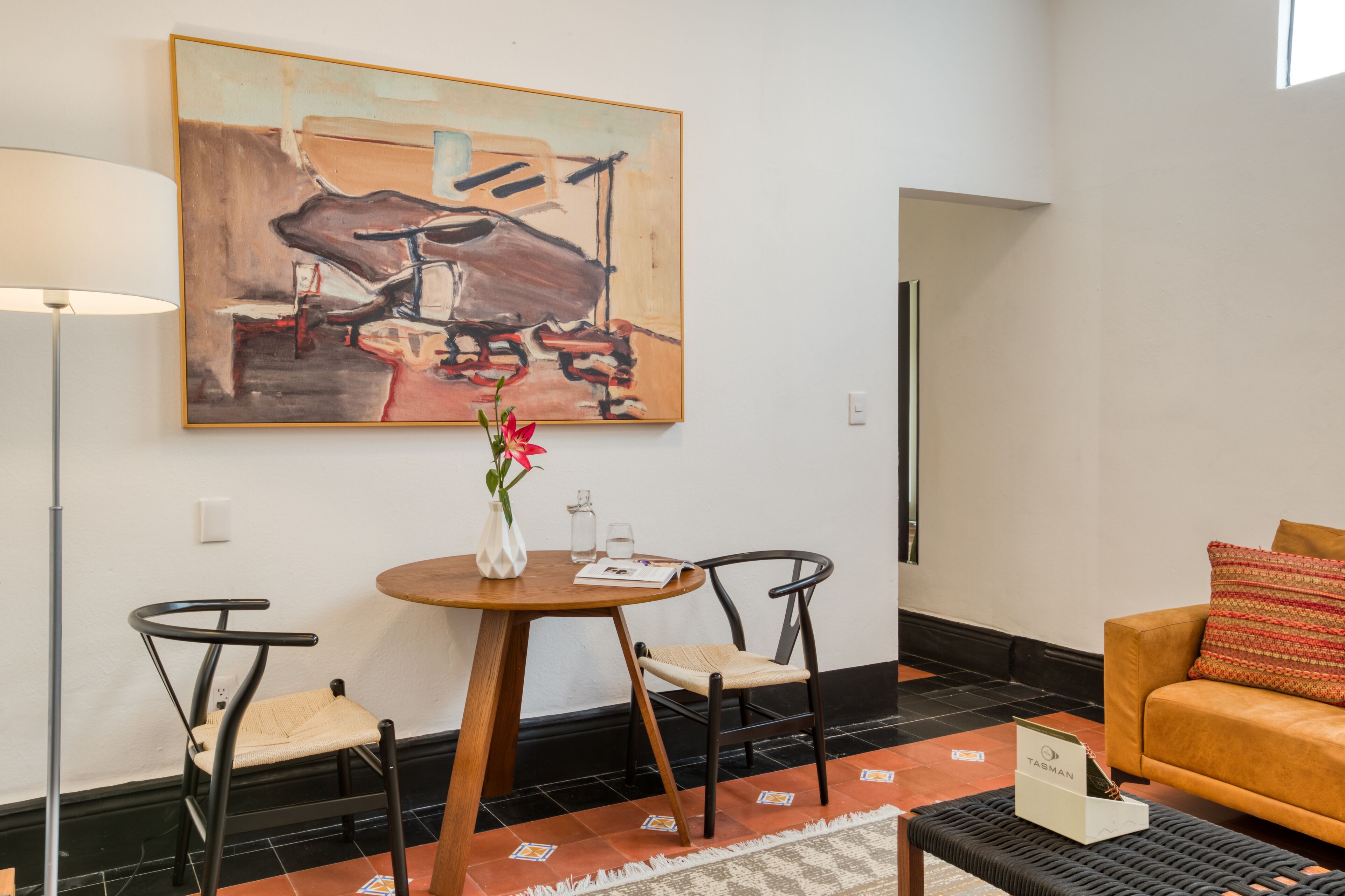 A modern room with a round wooden table, two chairs, a sofa, and a large abstract painting on the wall.