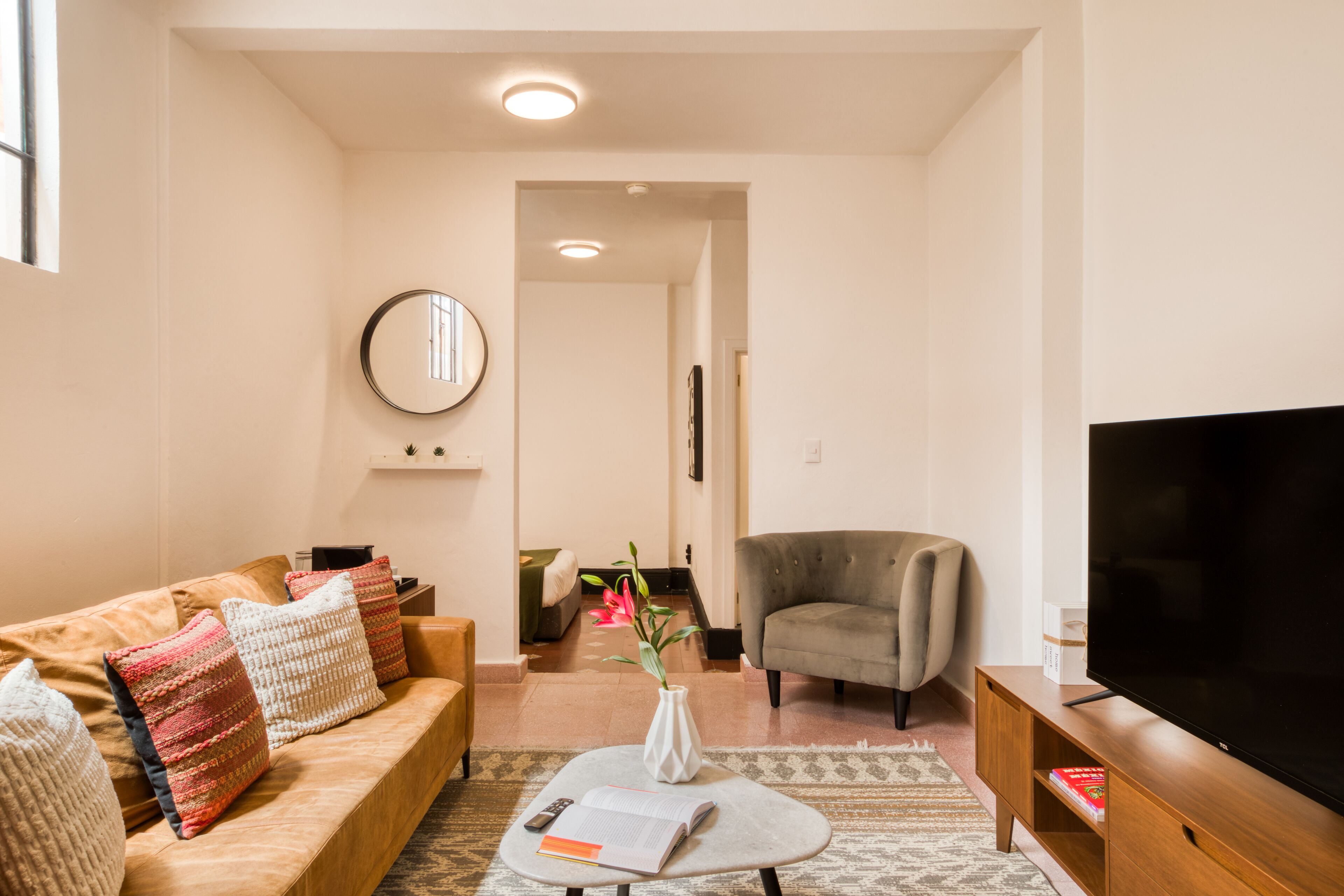 A living room with a sofa, armchair, TV, and a vase with flowers.