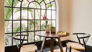 A room with a large arched window, a round wooden table, two wicker chairs, and a potted plant. - Santa Casa by Tasman (Mexico City)