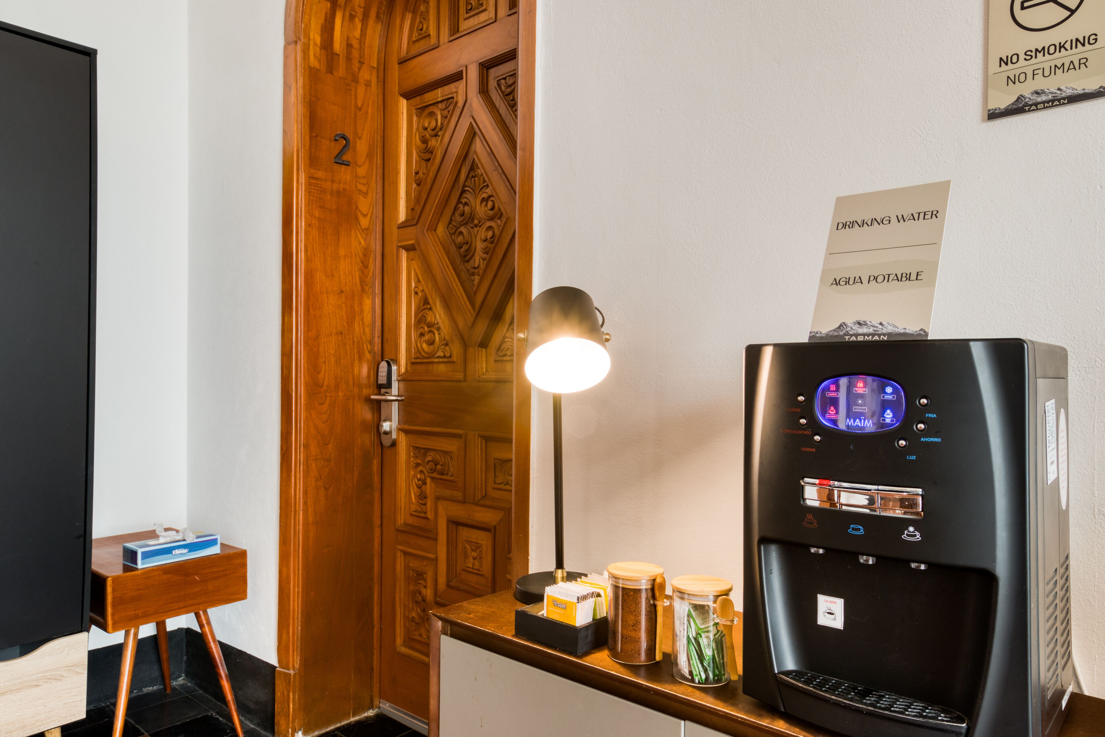 A room with a wooden door, a desk with a lamp, a water dispenser, and a sign indicating no smoking.