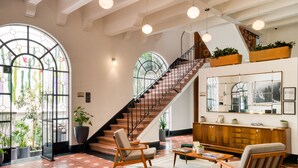 A spacious lobby with a wooden staircase, large windows with plant decorations, and a wooden reception desk. - Santa Casa by Tasman (Mexico City)