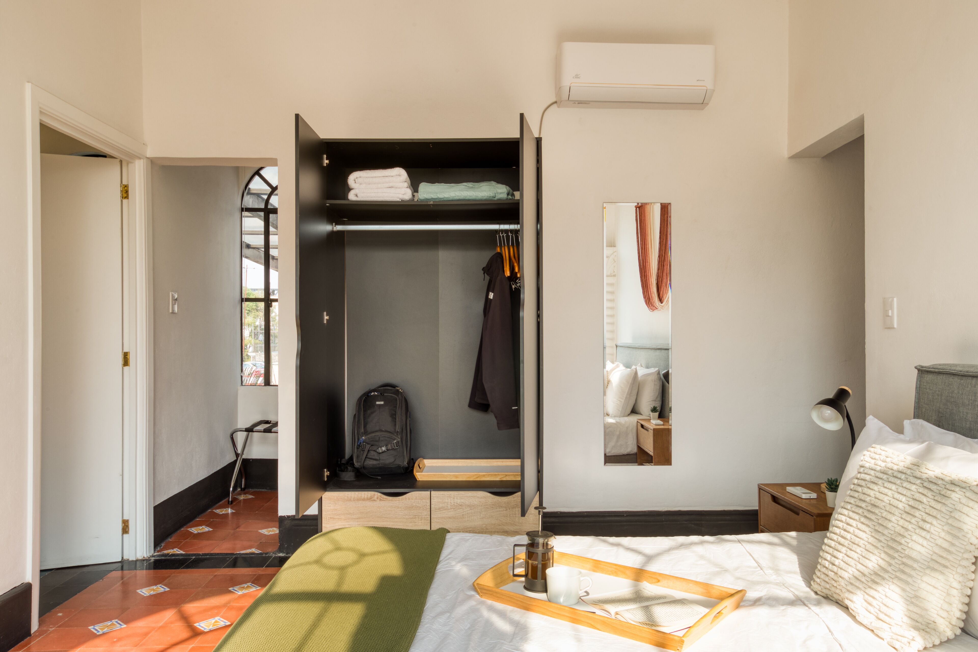 Een hotelkamer met een bed, nachtkastje, kledingkast en een spiegel.