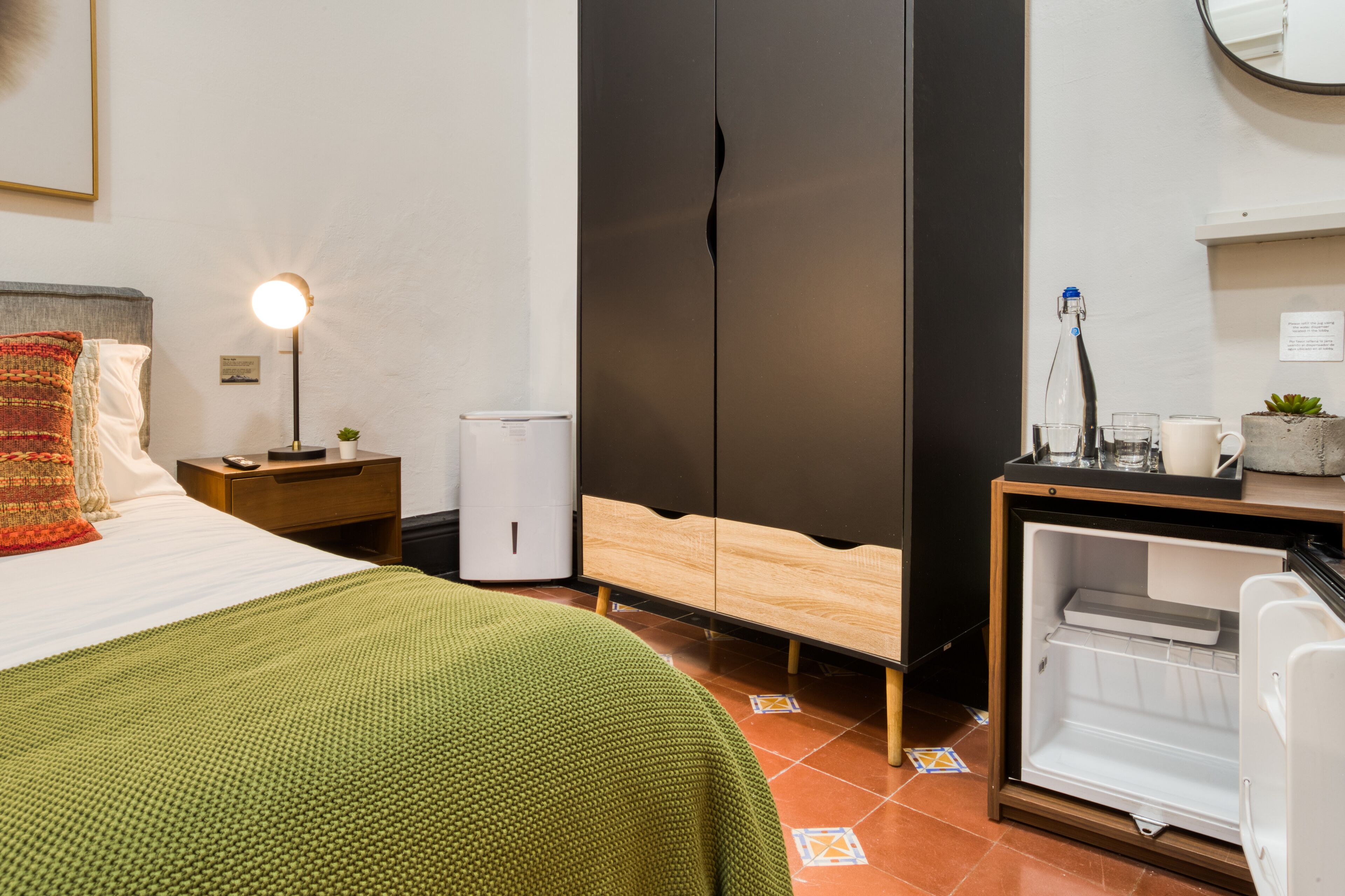Une chambre d’hôtel comprenant un lit, une table de chevet, un bureau avec une lampe, une armoire et un réfrigérateur.