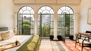 A hotel room with a large bed, a desk, and a view through arched windows. - Santa Casa by Tasman (Mexico City)