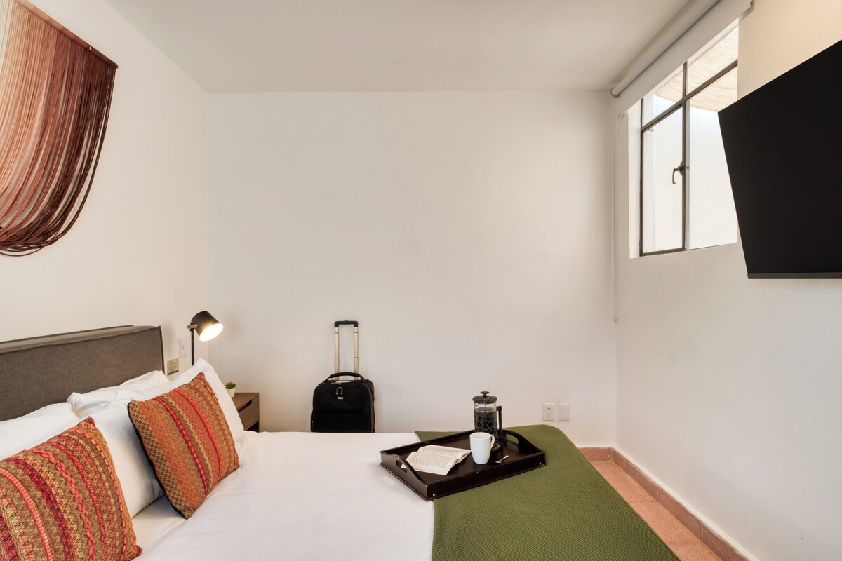 A hotel room with a bed, a suitcase, a tray with a cup and a book, and a window.