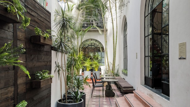 A narrow courtyard with wooden walls, potted plants, a seating area with a table and chairs, and a staircase leading to an upper level. - Santa Casa by Tasman (Mexico City)