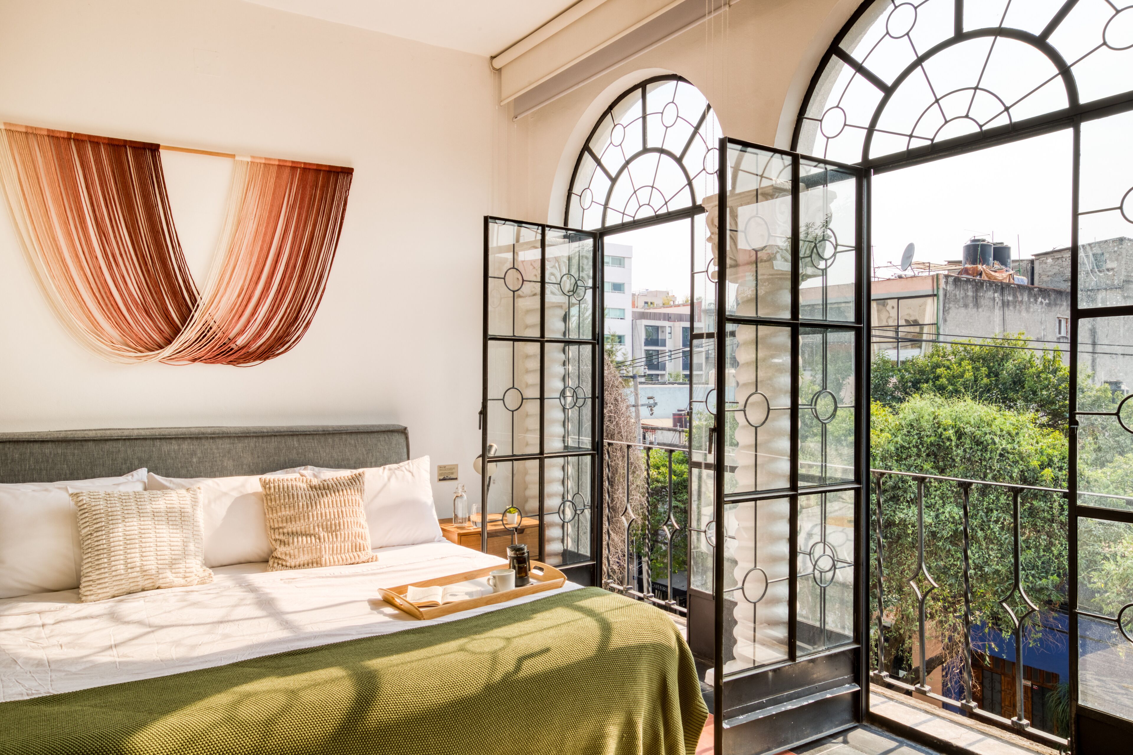 A bedroom with a large bed, a view of the city through arched windows, and a balcony with a railing.