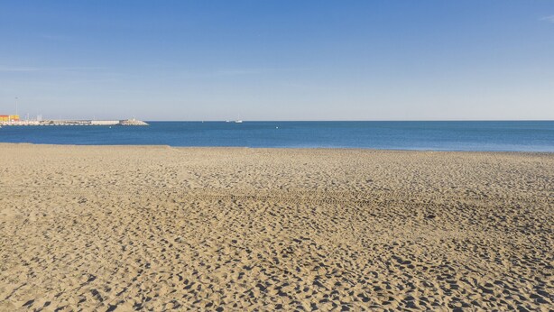 Une vaste plage de sable fin, sous un ciel bleu dégagé et une mer calme.