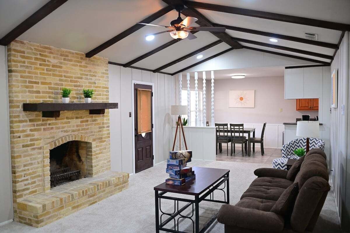A living room with a brick fireplace, a ceiling fan, and a dining area with a table and chairs.