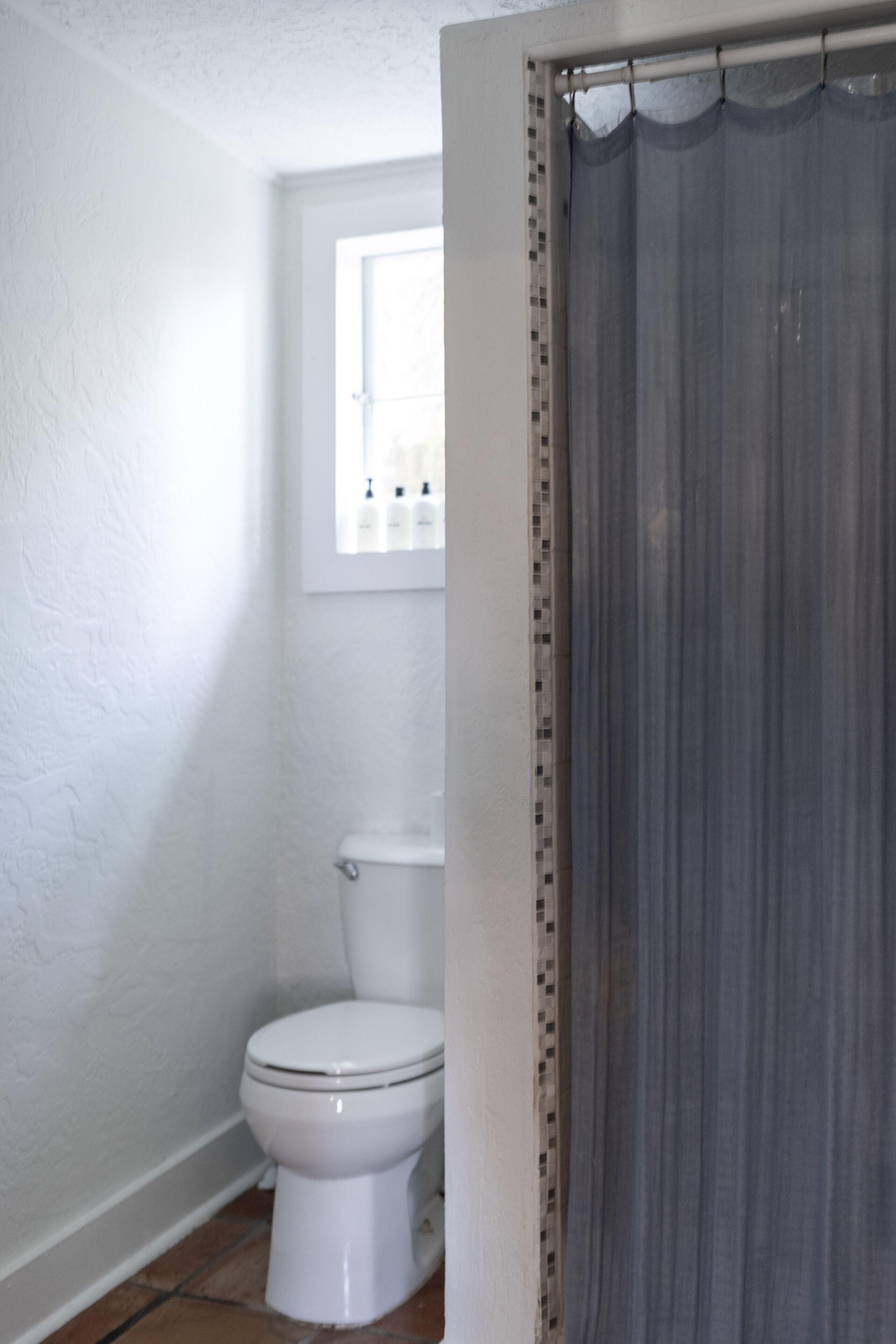 Une salle de bain avec des toilettes, une fenêtre au-dessus et un rideau de douche.