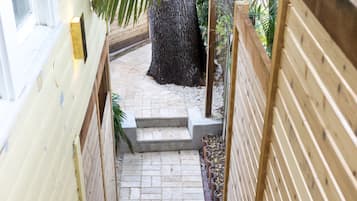 A wooden staircase leading to a covered outdoor area with a palm tree and a concrete bench.