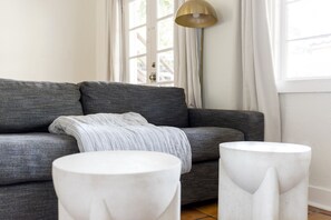 Una sala moderna con un sofá gris, una manta blanca y dos mesitas auxiliares blancas.